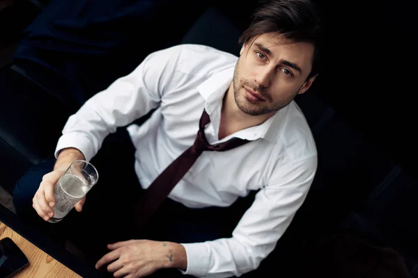 Schöner Mann im Anzug hält ein Glas Wasser in der Hand und blickt nach der Party in die Kamera — Stockfoto