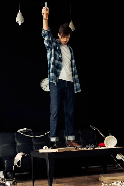 Drunk sleepy man standing on coffee table with bottle after party at home — Stock Photo