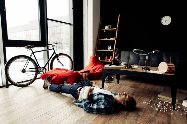 Drunk man lying on floor in messy living room after party — Stock Photo