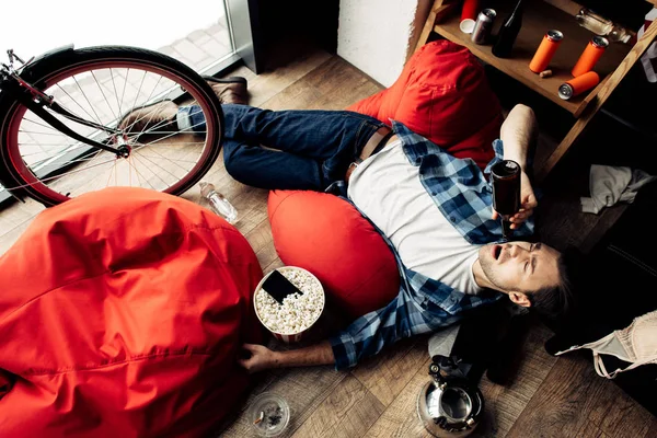 Пьяный мужчина лежит на бобовом мешке и пьет пиво — стоковое фото