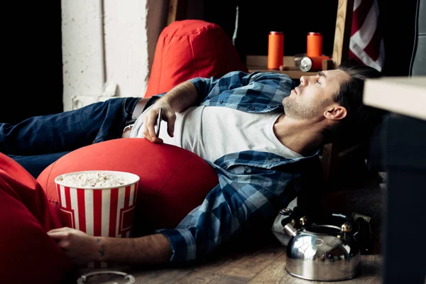 Сонный пьяница лежит на бобовом мешке и держит коробку попкорна — стоковое фото
