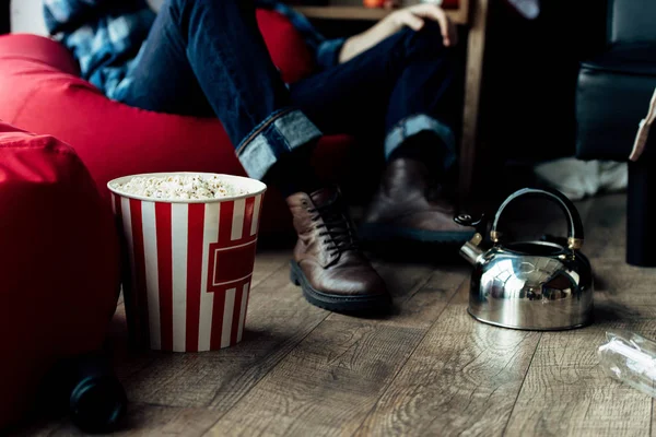 Vista ritagliata dell'uomo seduto sul sacchetto di fagioli vicino alla scatola di popcorn a casa — Foto stock
