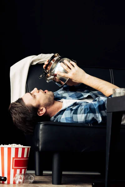 Красивий чоловік п'є від чайника, лежачи на дивані в безладному вітальні — стокове фото