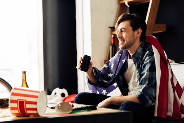 Cheerful man holding can with beer and sitting with american flag — Stock Photo