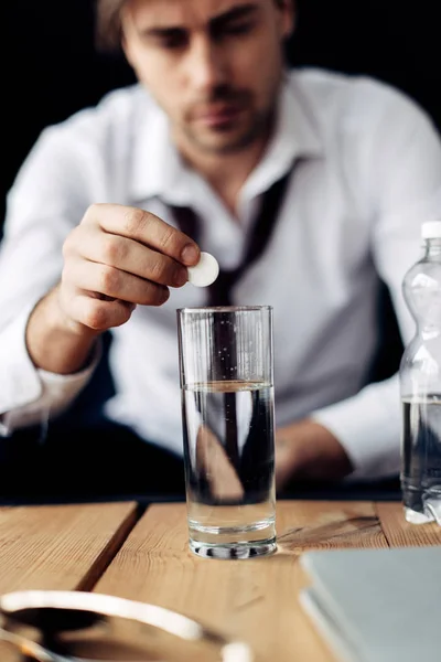 Enfoque selectivo del hombre poniendo aspirina en un vaso de agua - foto de stock