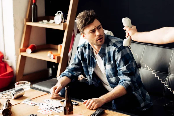 Cropped view of man holding retro phone in hand near drunk friend sitting on sofa — Stock Photo