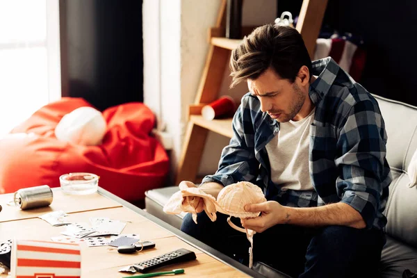 Uomo confuso guardando reggiseno mentre seduto sul divano dopo la festa — Foto stock