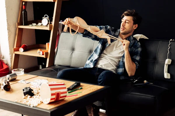 Sujetador hombre sosteniendo mientras está sentado en el sofá después de la fiesta - foto de stock