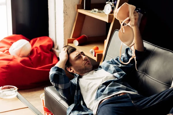 Uomo confuso reggiseno mentre sdraiato sul divano dopo la festa — Foto stock