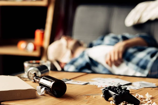 Foco seletivo de garrafa deitada na mesa de café com o homem dormindo com sutiã no rosto no fundo — Fotografia de Stock