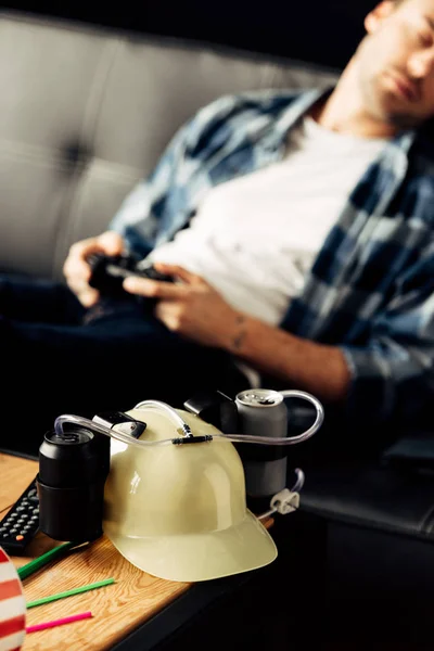 Selective focus of beer helmet with man sleeping and holding joystick on background — Stock Photo