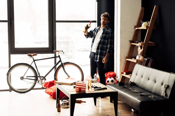 Man holding bottle of wine in messy living room after party — Stock Photo