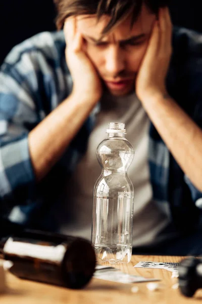 Enfoque selectivo de la botella vacía con el hombre que sufre de resaca en el fondo - foto de stock