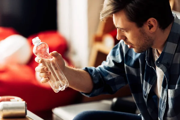 Homme souffrant de gueule de bois regardant la bouteille avec de l'eau à la maison — Photo de stock