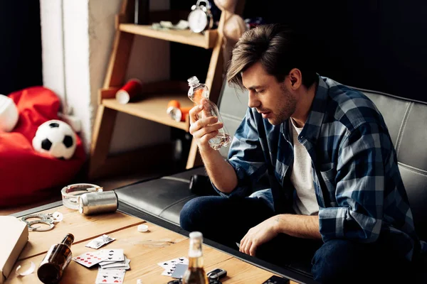 Man suffering from hangover holding bottle of water in hand and sitting on sofa — Stock Photo