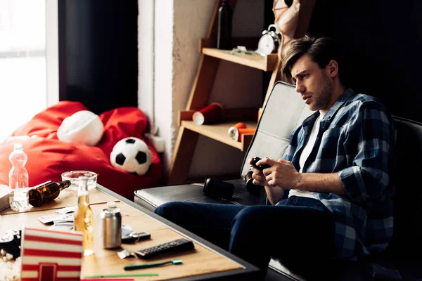 Tired man playing video game in messy living room — Stock Photo