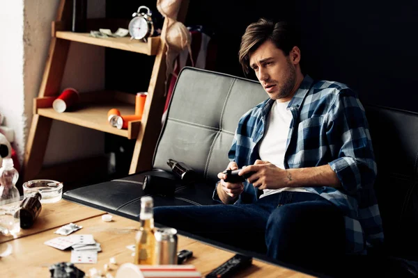 Hombre agotado jugando videojuego en la sala de estar desordenada - foto de stock