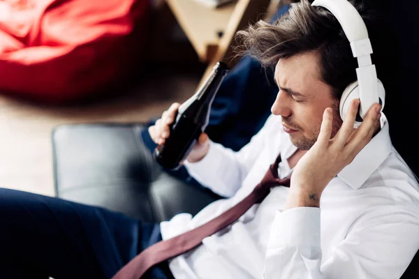 Homem de terno segurando garrafa e ouvir música em fones de ouvido — Fotografia de Stock