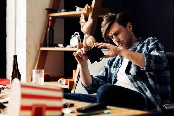 Selective focus of drunk man looking at wallet after party — Stock Photo