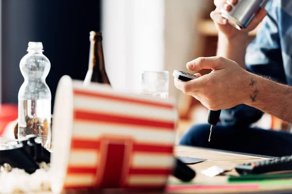 Cropped view of man holding remote control near drinks at home — Stock Photo