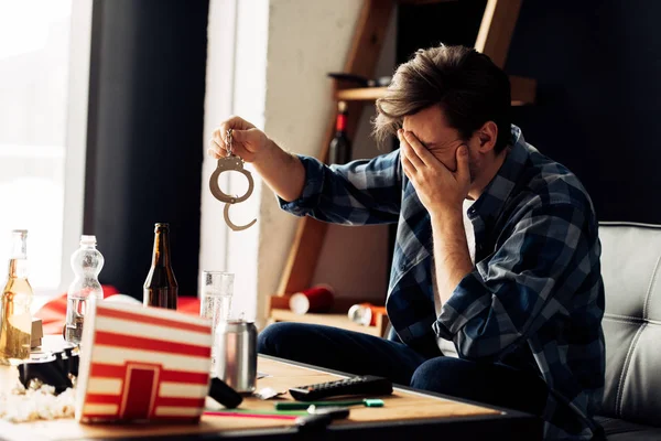 Uomo imbarazzato che copre il viso mentre tiene le manette dopo la festa — Foto stock
