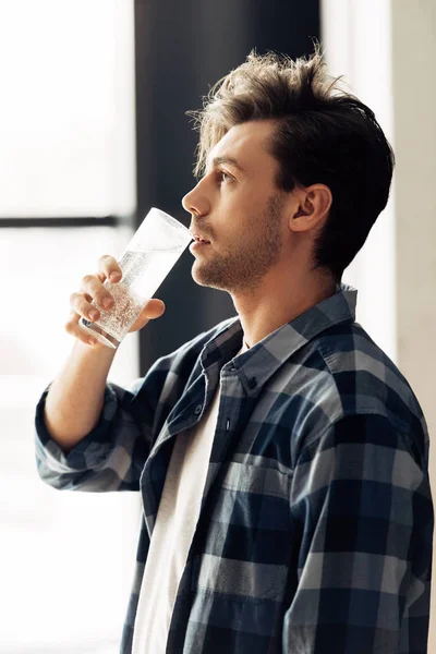 Bel homme tenant verre et eau potable après la fête — Photo de stock