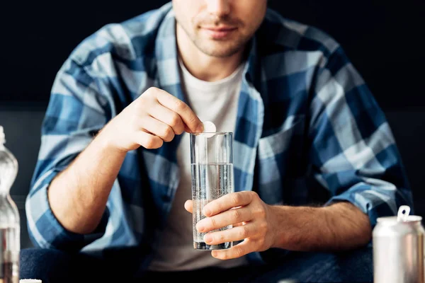 Обрезанный вид человека, страдающего от похмелья, держащего в руках аспирин и стакан воды — стоковое фото