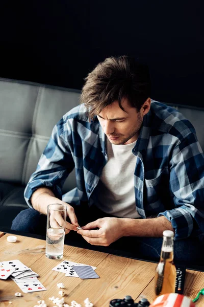 Человек смотрит на аспирин возле стакана воды в грязной гостиной — стоковое фото