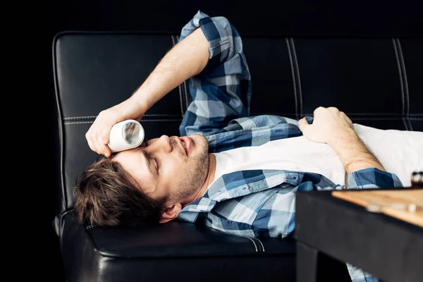Homme couché sur le canapé et tenant bouteille près de la tête après la fête — Photo de stock