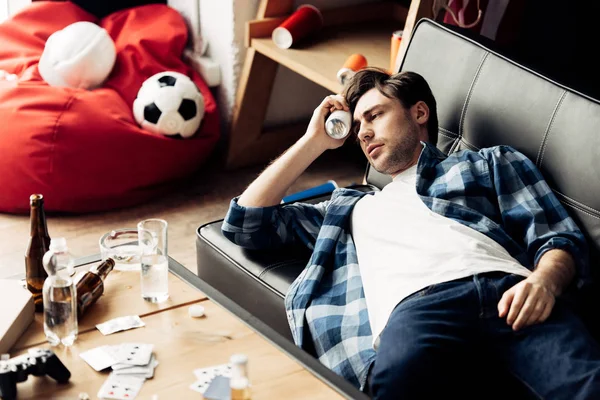 Homme couché sur le canapé et tenant bouteille près de la tête à la maison — Photo de stock