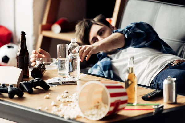 Selective focus of man taking glass of water on coffee table while lying on sofa — Stock Photo