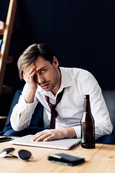 Enfoque selectivo del hombre cansado en traje sentado cerca de la botella y tener dolor de cabeza después de la fiesta - foto de stock