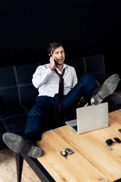 Man in suit sitting on sofa and talking on smartphone after party — Stock Photo