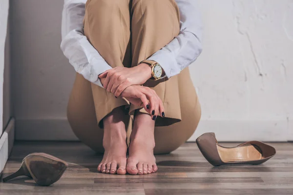 Cropped view of woman in white blouse and beige pants sitting on floor near wall at home, grieving disorder concept — Stock Photo