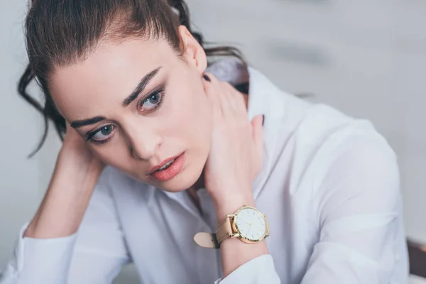 Portrait of sad woman in white blouse holding hands on neck in room, grieving disorder concept — Stock Photo