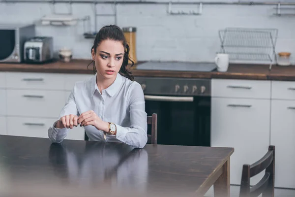 Verärgerte Frau in weißer Bluse sitzt am Holztisch in der Küche und trauert — Stockfoto
