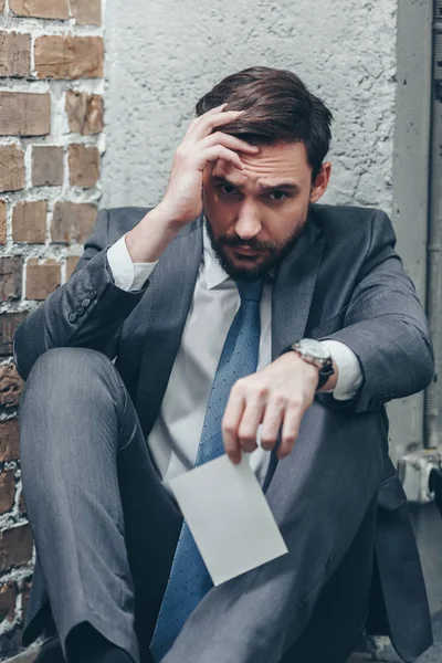 Bouleversé homme en costume gris assis sur le sol et tenant la photo sur fond brun texturé dans la chambre, concept de trouble de deuil — Photo de stock