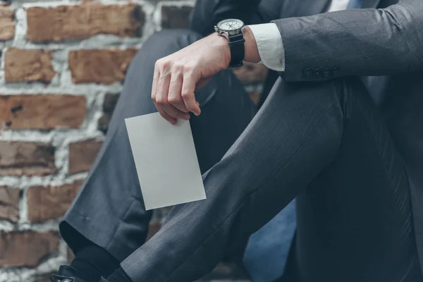 Vista recortada del hombre en traje gris sentado y sosteniendo foto sobre fondo de textura marrón en la habitación, concepto de trastorno de duelo - foto de stock