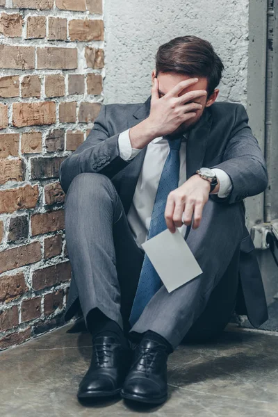 Mann im grauen Anzug sitzt auf dem Boden, hält Foto in der Hand und weint auf braunem Hintergrund im Raum, Konzept der trauernden Unordnung — Stockfoto