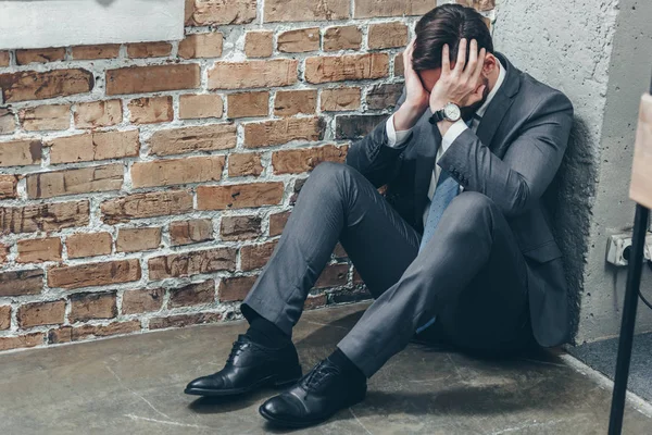 Грустный мужчина в сером костюме сидит в углу на полу и плачет на текстурированном фоне в комнате, скорбящее расстройство концепции — стоковое фото