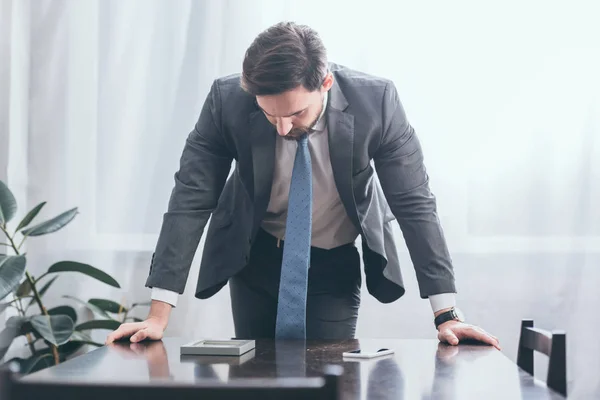 Homem triste em terno cinza em pé à mesa de madeira e olhando para a foto no quadro em casa, conceito de transtorno de luto — Stock Photo