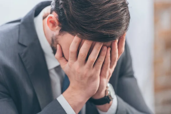 Bouleversé homme en costume gris couvrant le visage avec les mains dans la chambre, concept de trouble deuil — Photo de stock