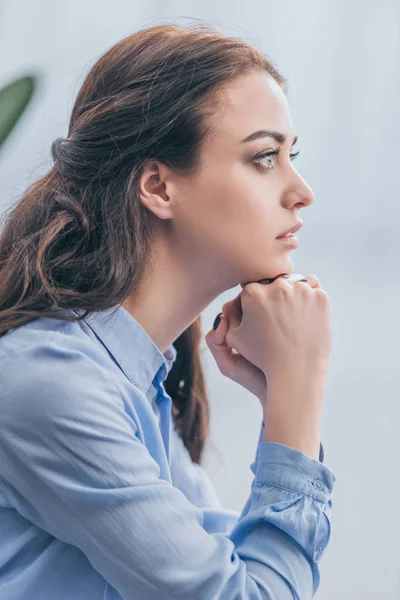 Mujer triste en blusa azul sentada y mirando a la distancia en casa, concepto de trastorno de duelo - foto de stock