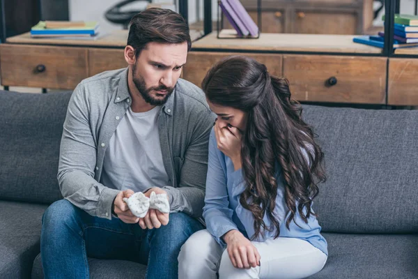 Woman sitting on couch and crying while sad man holding baby socks at home, grieving disorder concept — Stock Photo