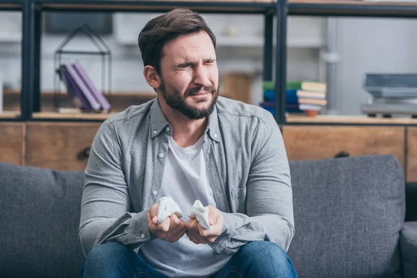 Man in grey shirt and blue pants sitting on couch, holding baby socks and crying in room, grieving disorder concept — Stock Photo