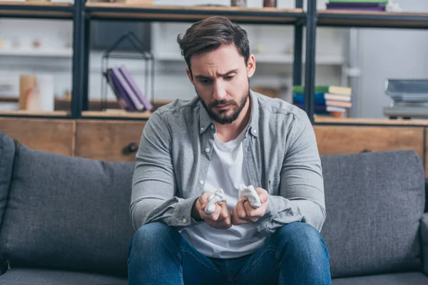 Sad man sitting on couch and holding baby socks at home, grieving disorder concept — Stock Photo