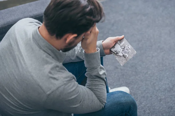 Hombre sentado en el sofá y mirando la foto en la habitación, concepto de trastorno de duelo - foto de stock