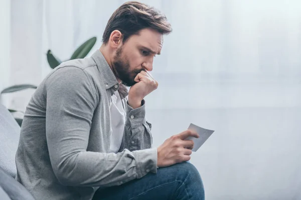 Trauriger Mann sitzt zu Hause vor Foto und trauert — Stockfoto