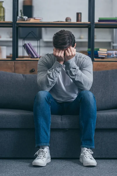 Uomo triste seduto sul divano e che copre il viso con le mani a casa, concetto di disturbo in lutto — Foto stock