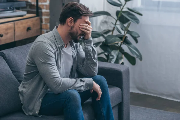 Чоловік сидить на дивані і плаче вдома, сумуючи за концепцією розладу — стокове фото